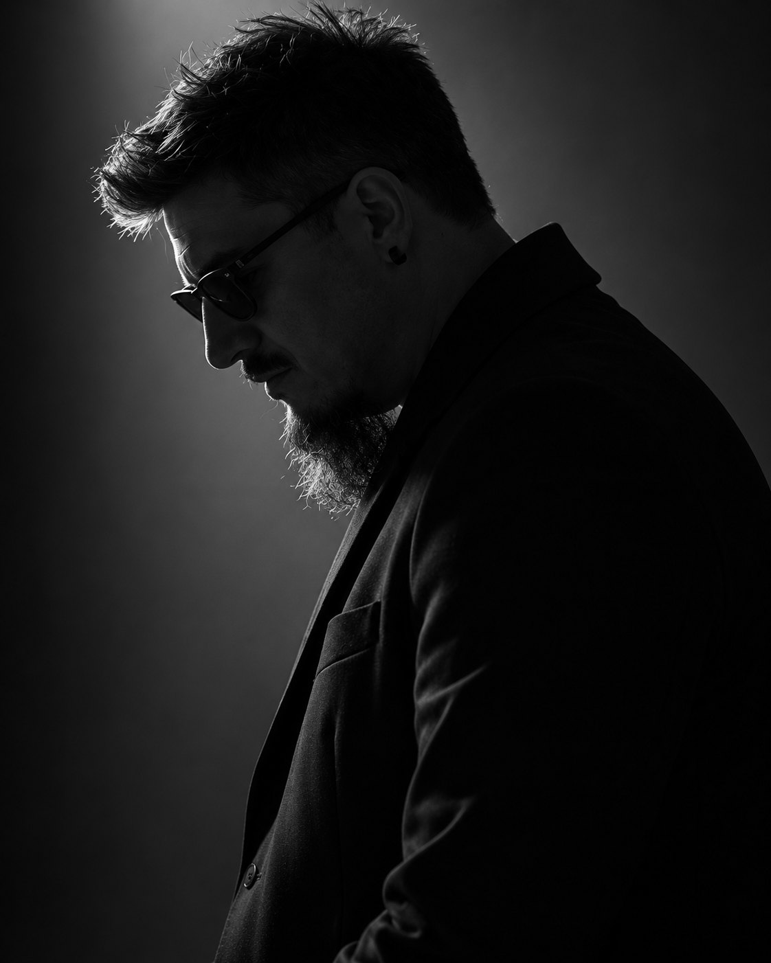 Aleksandar Žeželj in profile against a dark studio wall, lit from behind.